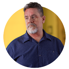 A man with a gray beard wearing a blue collar shirt looking off to the side